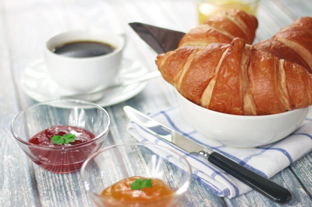 Delicious breakfast featuring croissants, coffee, and assorted jams on a rustic table.