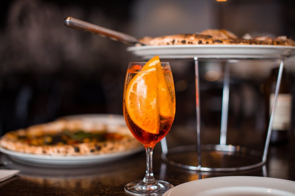 Close-up of Aperol Spritz with orange slices beside delicious pizza in a cozy restaurant setting.