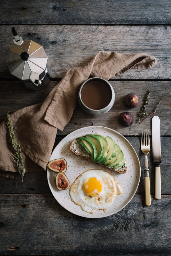 Top view of tasty breakfast from scrambled eggs and avocado under pepper near fresh hot coffee and silverware