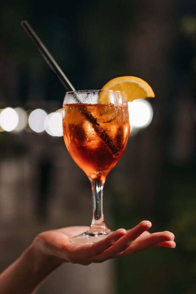 Close-up of Aperol Spritz cocktail held by a hand against blurred night background.